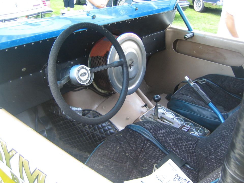 Interior of a custom drag car showing a steering wheel with a Ford logo, bucket seats, and a floor shifter