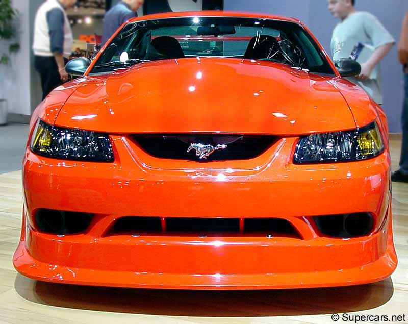 Front view of an orange Ford Mustang with a hood scoop and a pony emblem on the grille