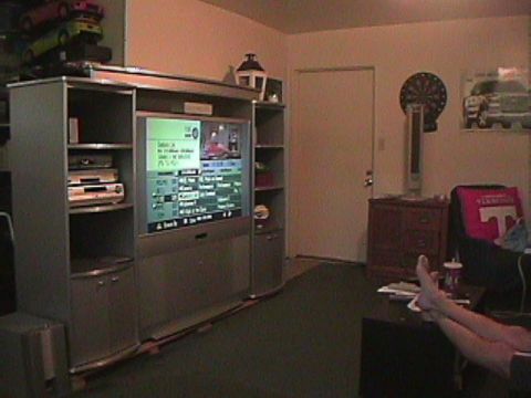 1994 Ford Bronco - A room is shown with a large entertainment center and a television displaying a menu, with a person's feet visible on a desk.