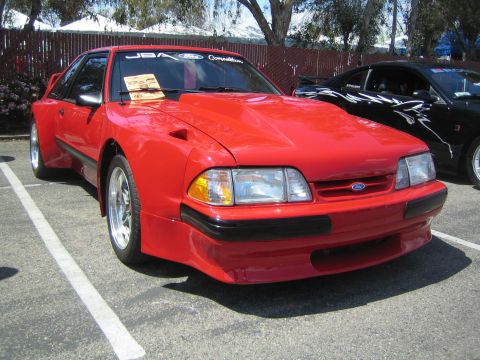 1968 Ford Mustang - A red Ford Mustang is parked in a lot, showing off its aftermarket hood scoop and custom body kit.