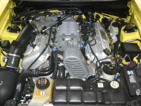 1994 Ford Probe - The engine bay of a yellow vehicle, a prominent supercharger and intricate plumbing.