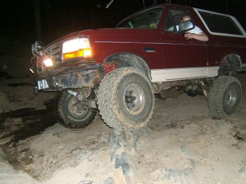 1993 Ford Bronco - Maroon and white Ford Bronco navigating a challenging rocky trail with its front passenger tire high off the ground.