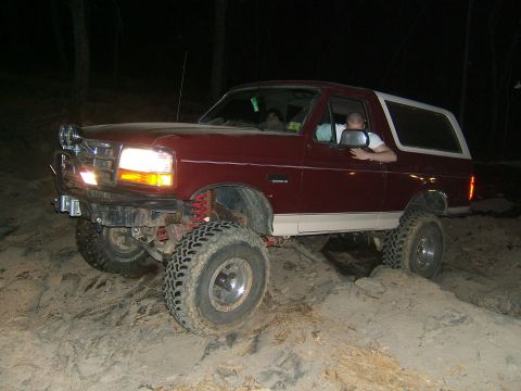 1993 Ford Bronco - This lifted Ford Bronco is navigating a challenging dirt terrain at night.