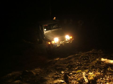 1993 Ford Bronco - Jeep Wrangler navigates an off-road trail at night, illuminated by its headlights.