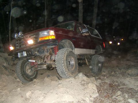 1993 Ford Bronco - A lifted Ford Bronco navigates a rocky trail in the dark, with another vehicle following behind.