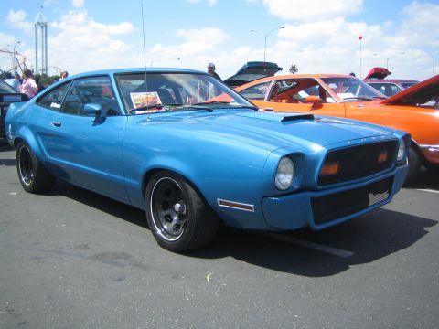 1968 Ford Mustang - A blue coupe with a hood scoop and black wheels is parked at an outdoor event.