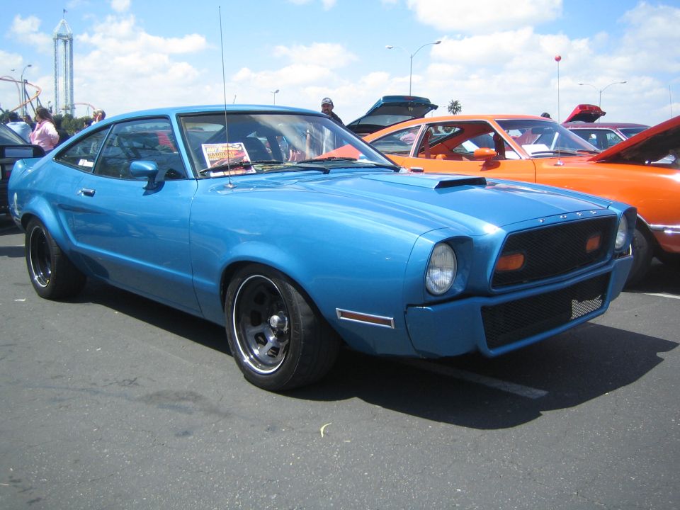 Blue coupe with a hood scoop and black wheels, seen from a 3/4 front angle