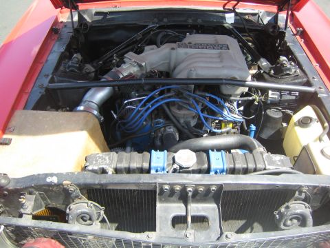 1968 Ford Mustang - The engine bay of a red car displays a "5.0 COBRA" intake manifold and blue spark plug wires.