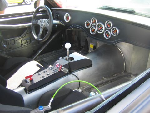 1968 Ford Mustang - The interior of a modified car features racing seats, a roll cage, and a dashboard filled with gauges.