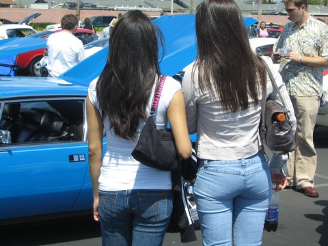 1968 Ford Mustang - Two women observe a blue car with its hood open at an outdoor car show.
