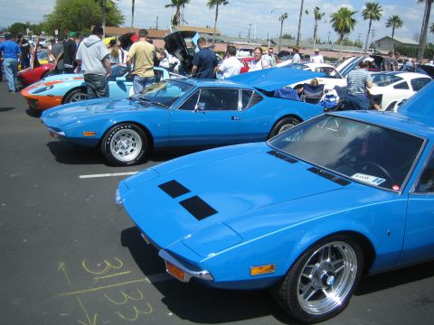 1968 Ford Mustang - Two blue De Tomaso Panteras are parked at a car show, with other vehicles and people in the background.