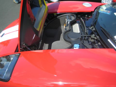 1968 Ford Mustang - The front trunk and engine bay of a red car are exposed with the hood open, revealing storage and mechanical parts.