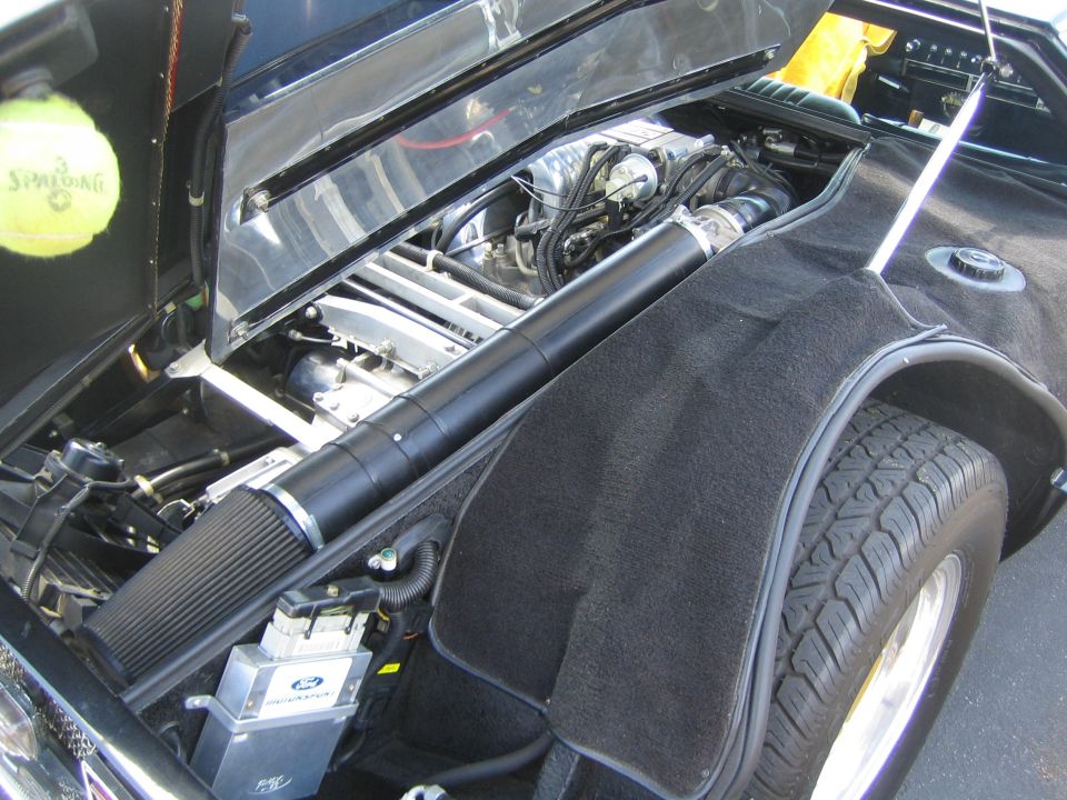 Car's engine bay with a tennis ball on the left. Air intake tube runs across the engine