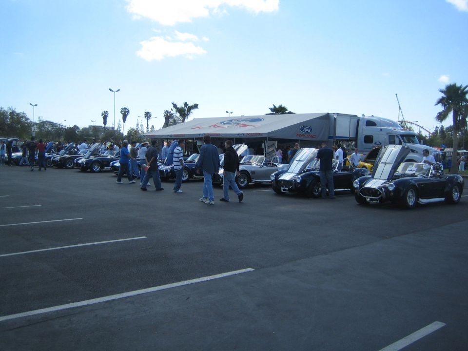 Cars lined up under a Ford tent, some with hoods open. People milling around