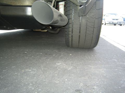 1968 Ford Mustang - A close-up view of a vehicle's exhaust pipe and tire, with another car visible in the background.