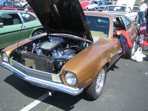 1968 Ford Mustang - A brown 1970s Ford Pinto is displayed with its hood open, showing the engine bay. Other vehicles are parked nearby.