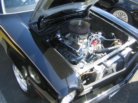 1968 Ford Mustang - The engine bay of a black car with a yellow stripe on the fender is open for viewing.