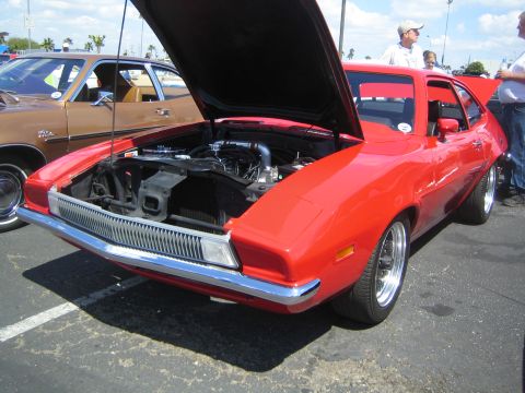 1968 Ford Mustang - A red sports car is parked with its hood up, revealing the engine compartment. Another vehicle is visible to the left.