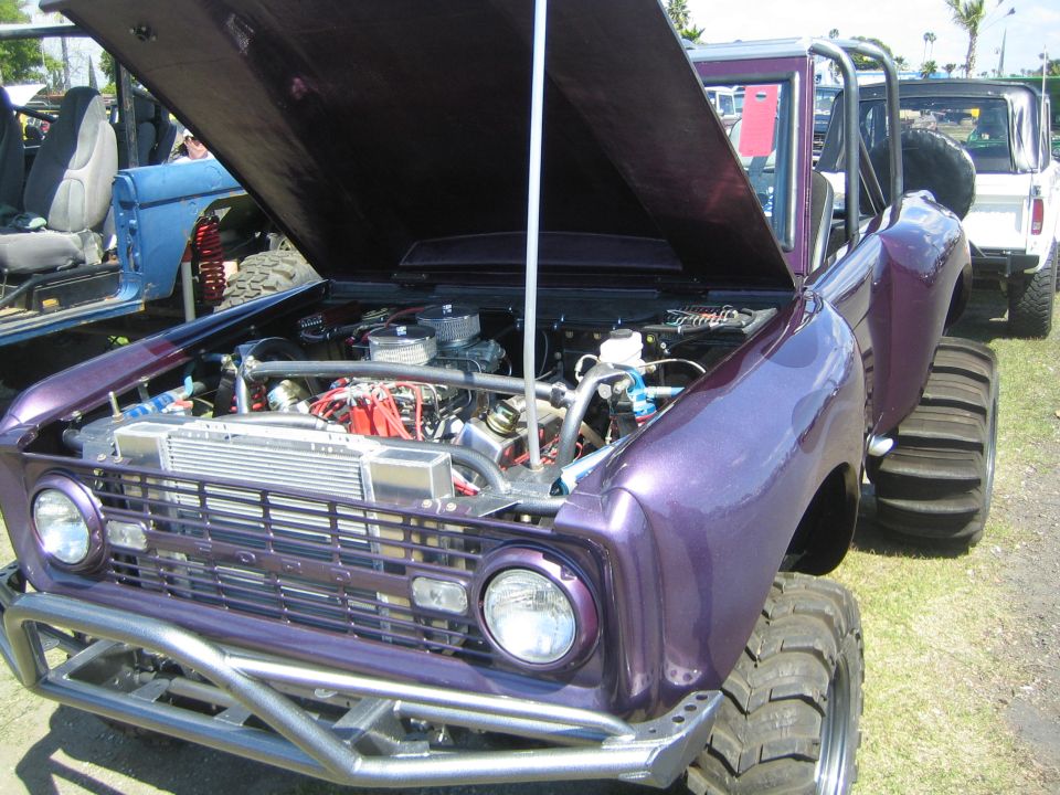 Customized purple Ford Bronco, hood open showing engine and aftermarket radiator. Another Bronco is visible behind it