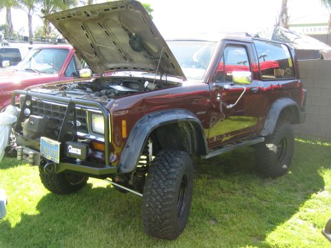 1968 Ford Mustang - A maroon Ford Bronco II is parked on grass with its hood open, its engine and aftermarket bull bar.