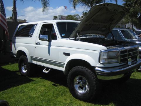 1968 Ford Mustang - A white Ford Bronco is parked on grass with its hood up, showing the engine bay.