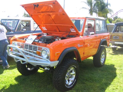 1968 Ford Mustang - An orange Ford Bronco is displayed with its hood up, parked on grass next to another vehicle.