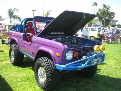 1968 Ford Mustang - A modified purple Ford Bronco is displayed with its hood open at an outdoor car show.