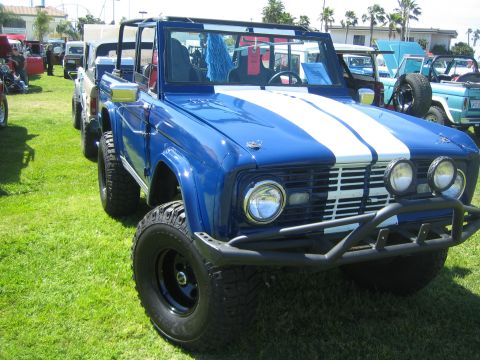 1968 Ford Mustang - A blue first-generation Ford Bronco with white racing stripes is parked on a grassy field alongside other vehicles.