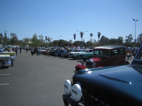 1968 Ford Mustang - A car show features rows of classic vehicles under a clear blue sky, with a dark green SUV prominently displayed in the foreground.