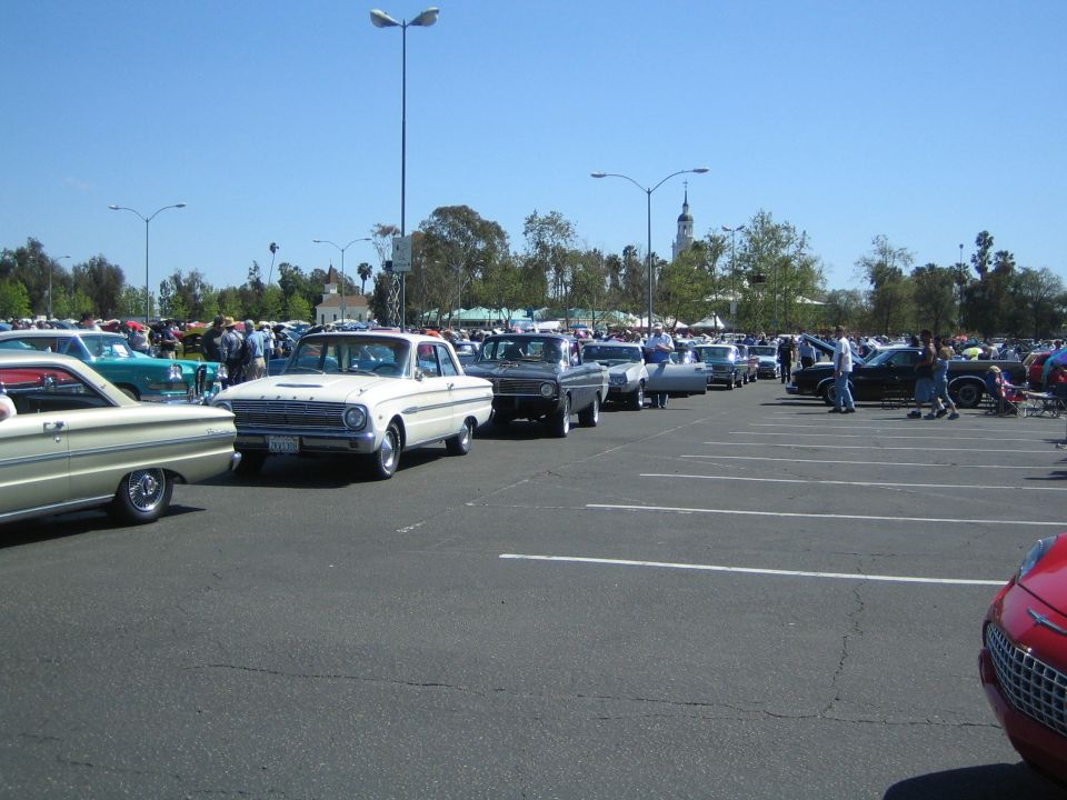 Line of classic cars parked in a lot, including a white 1963 Ford Falcon and a cream-colored car in the foreground