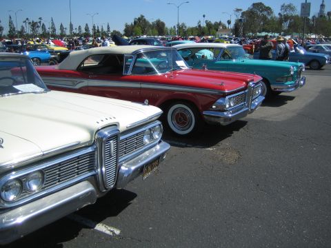 1968 Ford Mustang - A row of classic American cars are parked at an outdoor event, with more vehicles visible in the background.