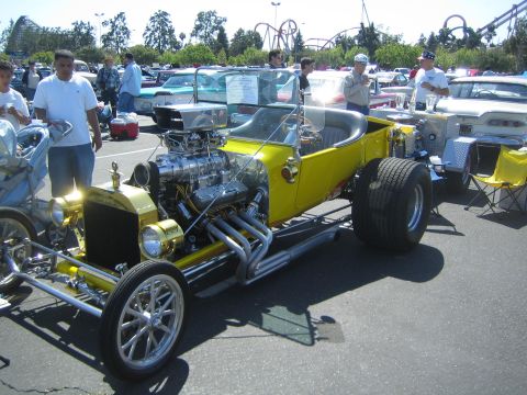 1968 Ford Mustang - A bright yellow hot rod with a prominent supercharger and exhaust pipes is parked at an outdoor car show.
