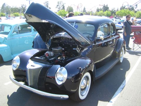 1968 Ford Mustang - A classic dark coupe is displayed with its hood open, revealing the engine bay. Another vintage car is visible beside it.