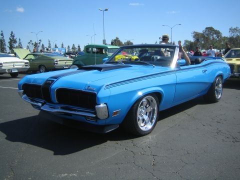 1968 Ford Mustang - A bright blue 1969 Mercury Cougar convertible, distinguished by its black racing stripes and prominent hood scoop, is showcased at an outdo…