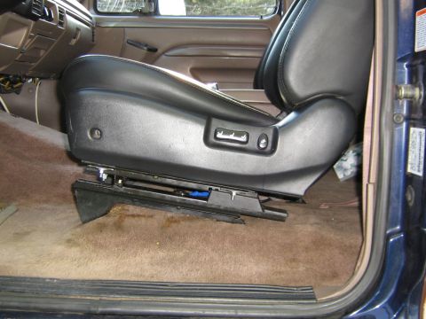 1995 Ford Bronco - The interior of a vehicle features a black leather seat with visible power controls and a tan carpet floor.