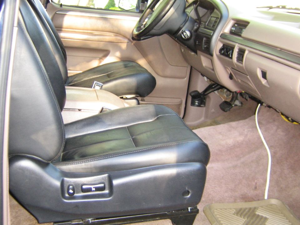 Black leather bucket seats and tan dash inside a Ford Bronco, seen from the open passenger door