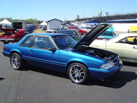 1986 Ford Bronco - Blue 1987 Ford Mustang coupe at an outdoor car event.