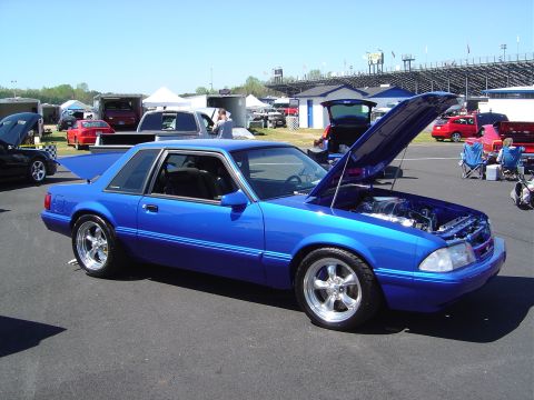 1986 Ford Bronco - A blue coupe, likely a Ford Mustang from the mid-1980s, is displayed with its hood open at an outdoor event.