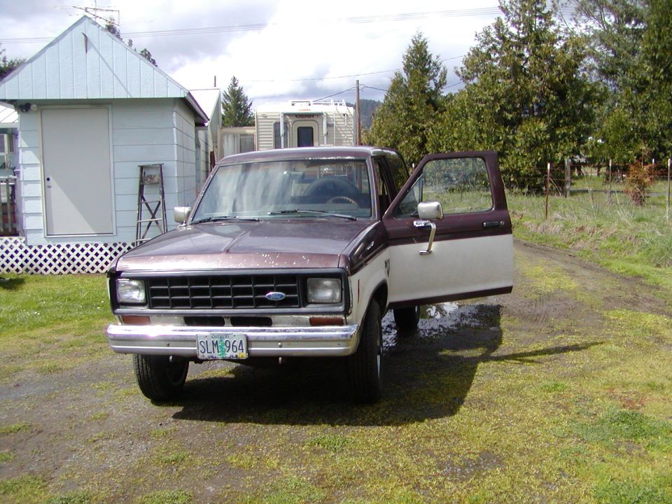 Brown and white Ford Ranger pickup truck with driver's door open, parked on a dirt road