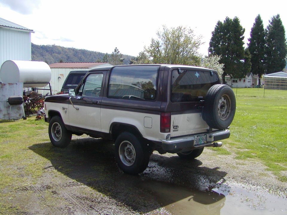 1987 Ford Bronco II, two-tone white and brown, with spare tire mounted on the rear door. Parked on a dirt lot