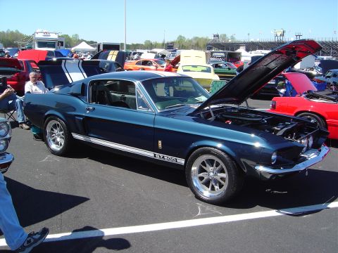 1986 Ford Bronco - A dark blue 1967 Shelby GT500 is displayed with its hood open at an outdoor car event.