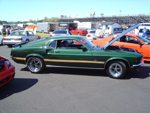 1986 Ford Bronco - A classic green Mustang Mach 1 is displayed at an outdoor event with a grandstand in the background.