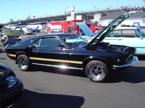 1986 Ford Bronco - A black 1969 Ford Mustang coupe is displayed with its hood open at an outdoor car show.