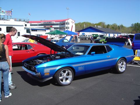 1986 Ford Bronco - A blue 1971 Ford Mustang Mach 1 is displayed with its hood open at an outdoor car show, alongside other vehicles.