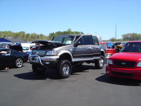 1986 Ford Bronco - Lifted gray Ford F-150 pickup truck at an outdoor car show.