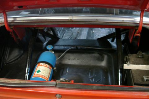 1981 Ford Mustang - The trunk of a red car reveals a NOS tank, battery, and roll cage, suggesting performance modifications.