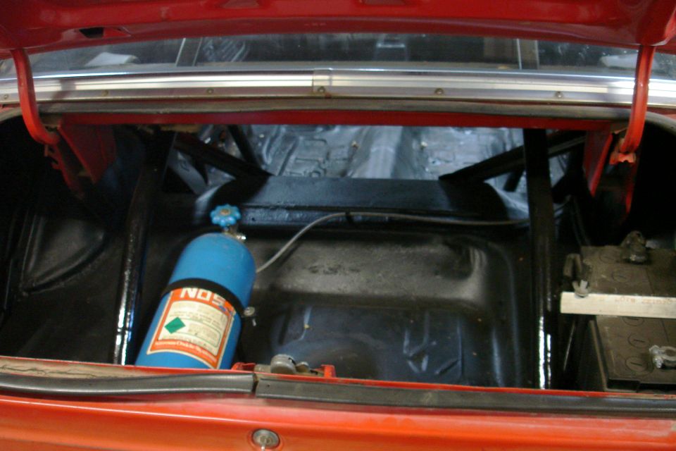 Red car trunk interior with a blue NOS tank, battery, and roll cage