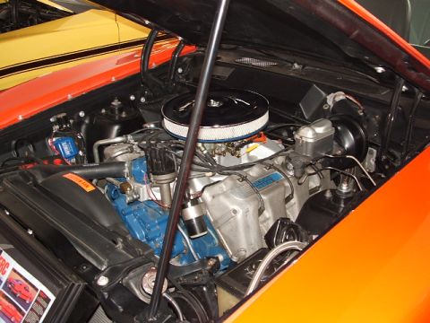 1966 Ford Ranchero - The engine bay of an orange vehicle reveals a V8 engine, with another car visible behind it.