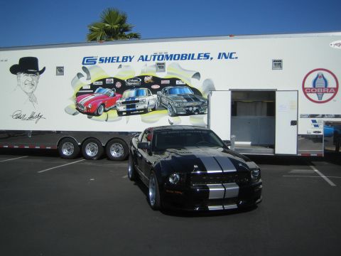 1968 Ford Mustang - A modern Ford Mustang is parked in front of a trailer Shelby Automobiles branding and graphics of classic cars.