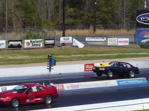 1986 Ford Bronco - Two Ford Mustangs race down a drag strip, one with its front wheels off the ground.